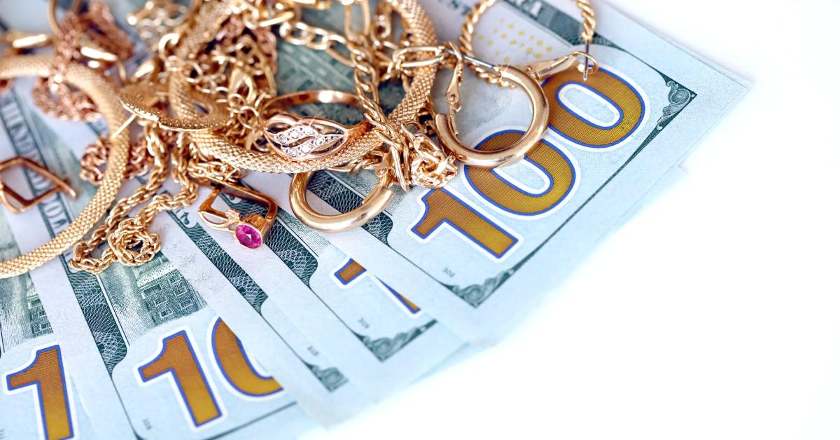 Multiple gold items, including rings, earrings, and bracelets, piled on top of multiple hundred-dollar bills.